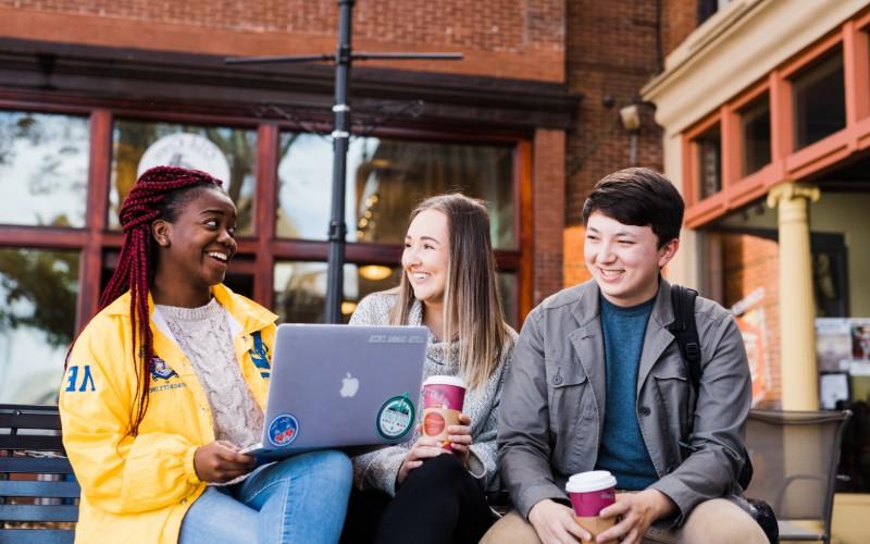 three students chatting and studying on the laptop in front of cafe 