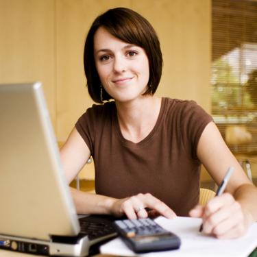 Female looking at the camera, sitting at her desk holding a pen with her computer in front of her.