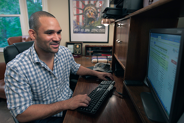 Man in blue button down sitting at his desk working on his computer.